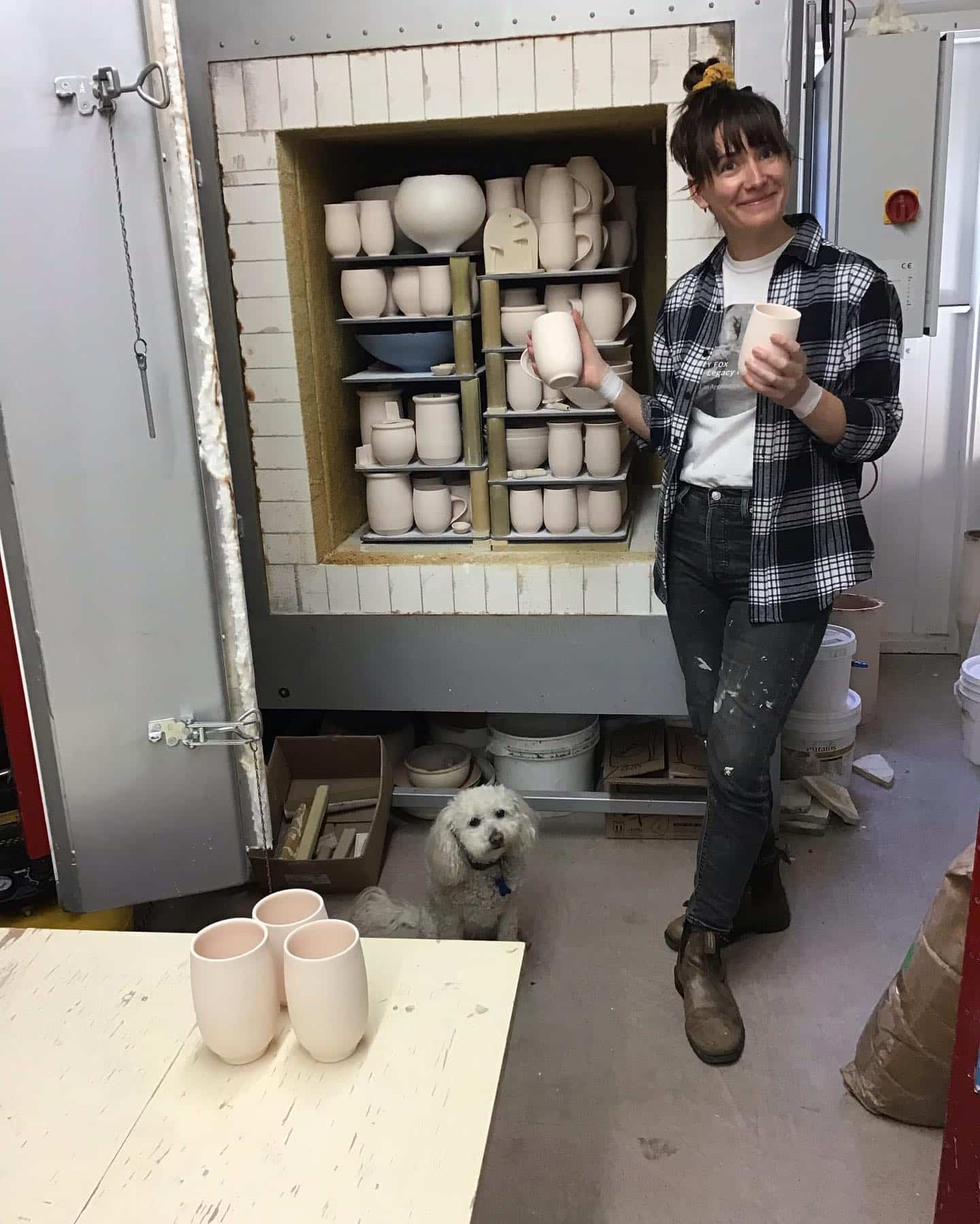 Apprentice Sarah Wilson in front of the kiln holding two mugs